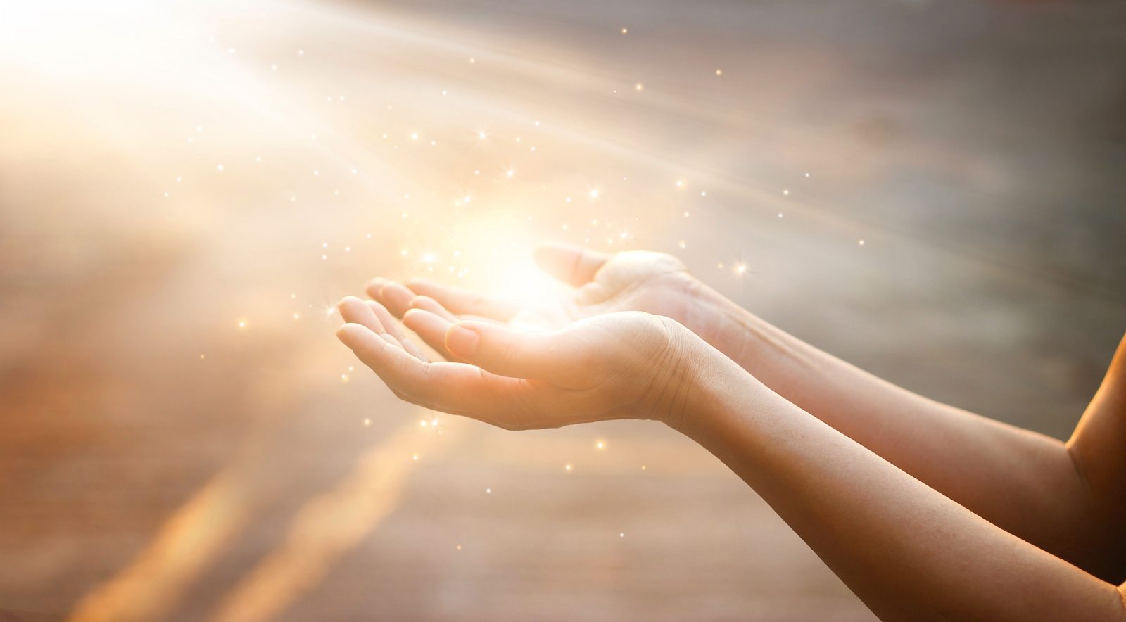 Cupped hands full of light radiating outward at sunset