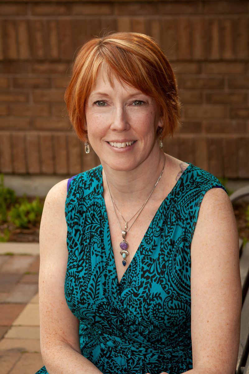 Chris MacPherson smiling warmly in a teal and green patterned dress